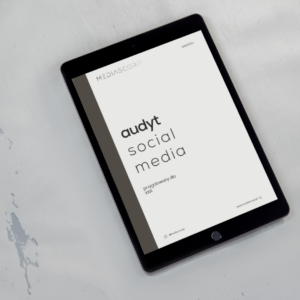 Tablet z wyświetlonym tytułem audyt social media na białym tle z logo firmy w rogu ekranu