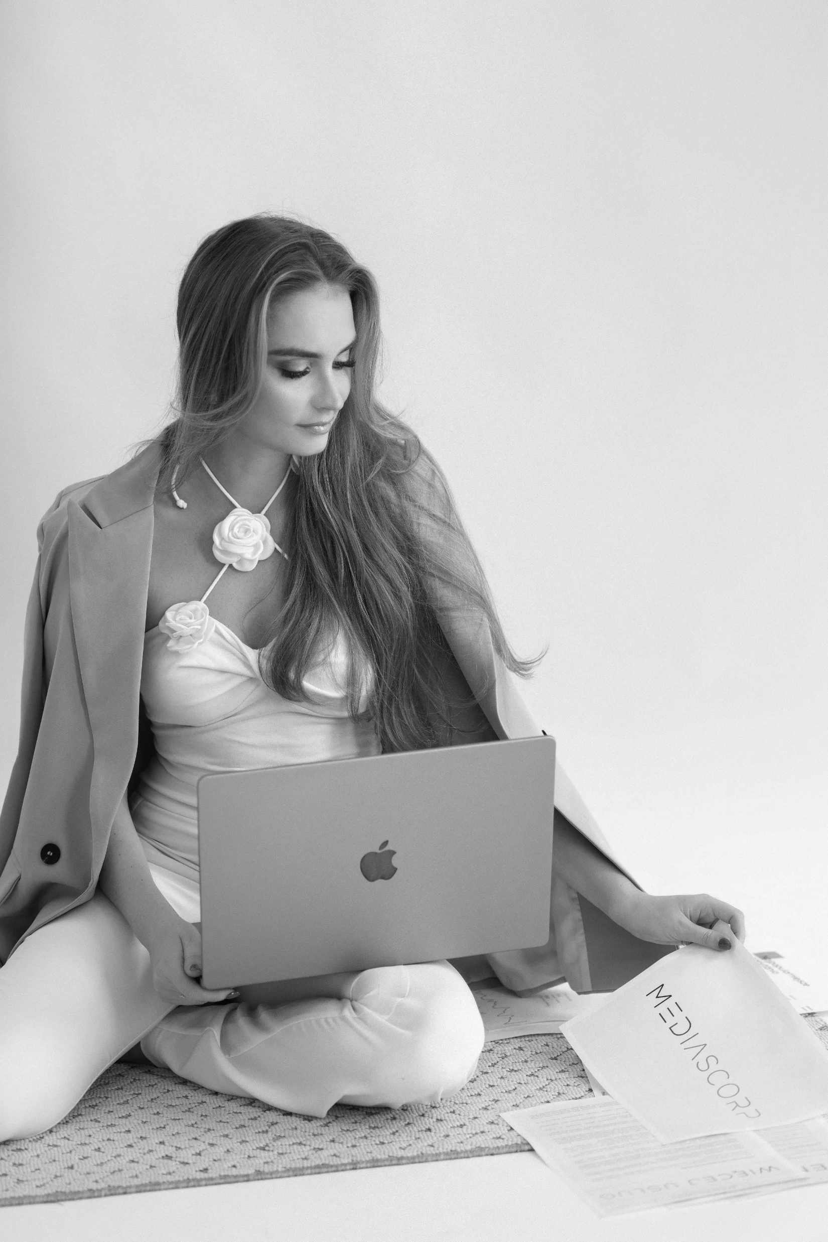 Kobieta w eleganckiej sukience z kwiatami pracuje na laptopie siedząc na podłodze z dokumentami